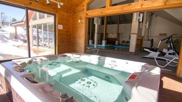A wooden cabin with a hot tub, exercise equipment, and a view of a snowy landscape. - Trail Creek 54 (Killington)