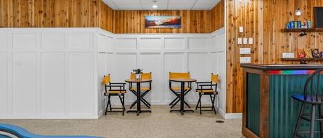 A pool area with a wooden wall, a small table with chairs, and a bar counter with snacks.