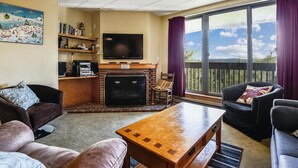 A living room with a fireplace, a flat-screen TV, and a large window with a view of the outdoors. - Pinnacle F21 (Killington)