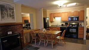 A compact kitchen with wooden cabinets, a dining table with chairs, and a fireplace. - Whiffletree B8 (Killington)