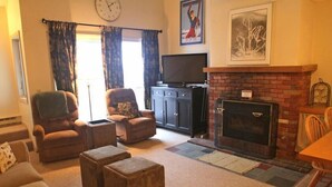 A living room with a fireplace, a television, and a clock on the wall. - Whiffletree B8 (Killington)