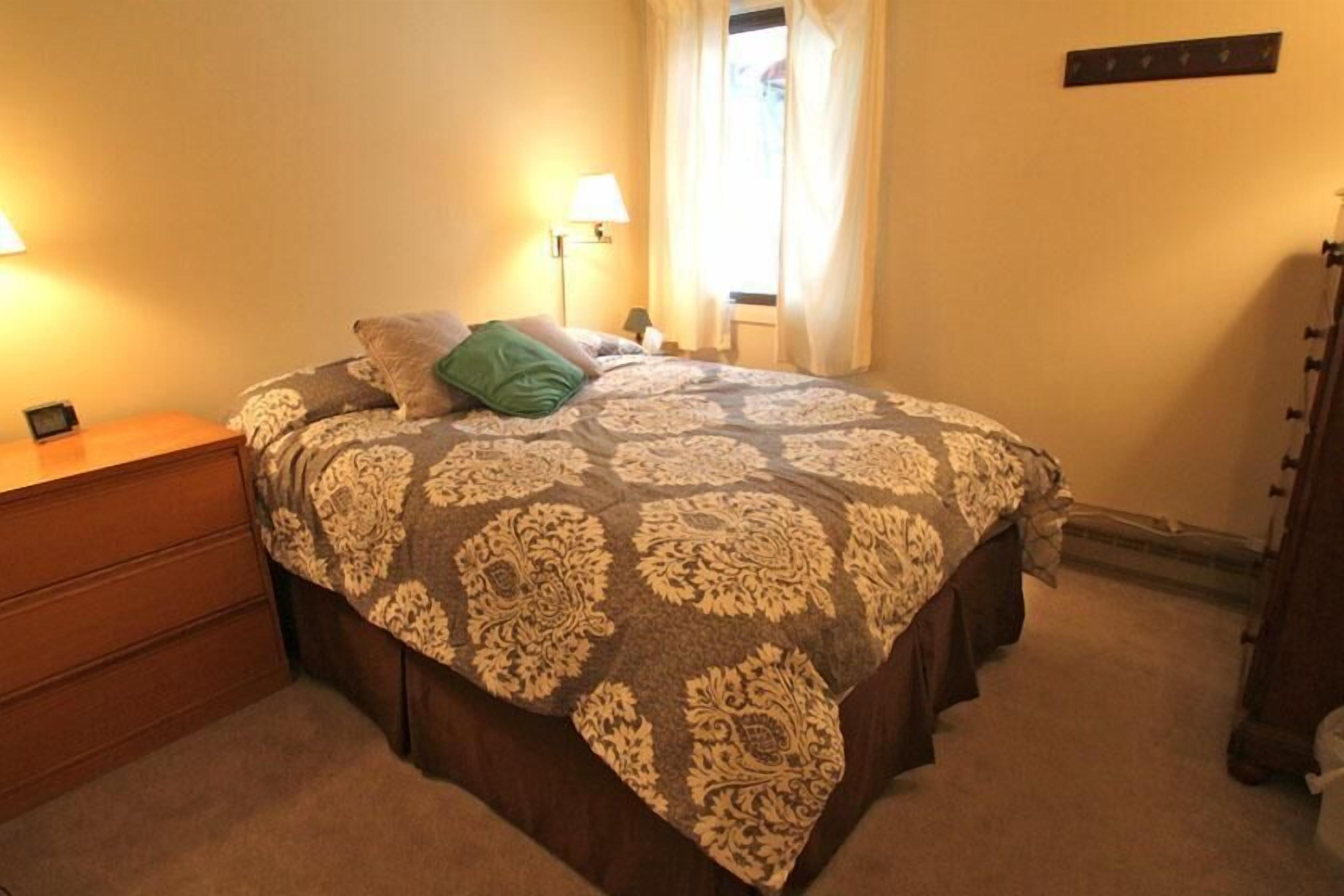 A bedroom with a bed, bedside tables, a lamp, and a window with curtains.