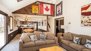Una sala de estar acogedora con un conjunto de sofá, una mesa de centro y un comedor con mesa y sillas de madera. Se ve una bandera canadiense y un letrero de precaución.