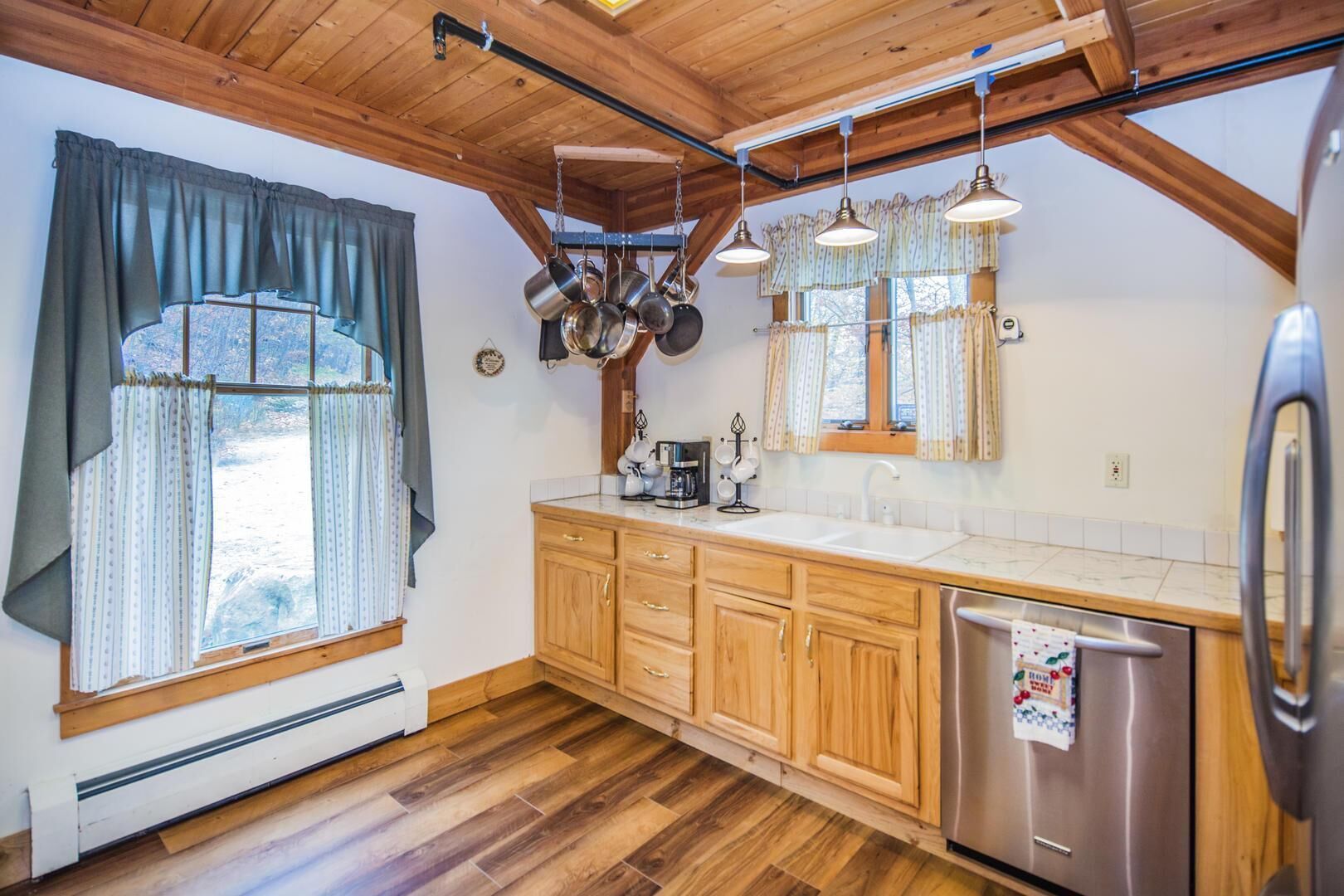 Una cocina con armarios de madera, un refrigerador de acero inoxidable y ollas colgando.