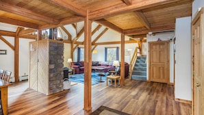A spacious living area with wooden beams, a stone fireplace, and a staircase leading to another level. - Viewmont Chalet (Killington)