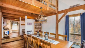 A dining area with a wooden table and chairs, a chandelier, and a view of trees through a window. - Viewmont Chalet (Killington)