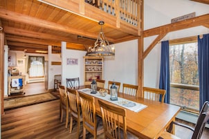 Comedor con mesa y sillas de madera, una araña y vista a los árboles por una ventana.