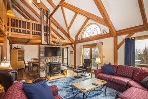 A spacious living room with a stone fireplace, wooden beams, a high ceiling, and a cozy seating area. - Viewmont Chalet (Killington)