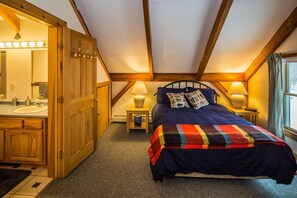 A bedroom with a bed, a nightstand, a lamp, a window, and a bathroom with a sink and mirror. - Viewmont Chalet (Killington)
