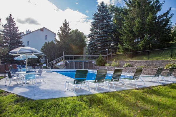 A swimming pool with lounge chairs and umbrellas, surrounded by trees and a building. - Pinnacle F8 (Killington)