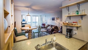 A compact kitchen with a granite countertop, a sink, and a coffee maker. There is a dining area with a table and chairs, and a living area with a couch and a bookshelf. - Pinnacle F8 (Killington)