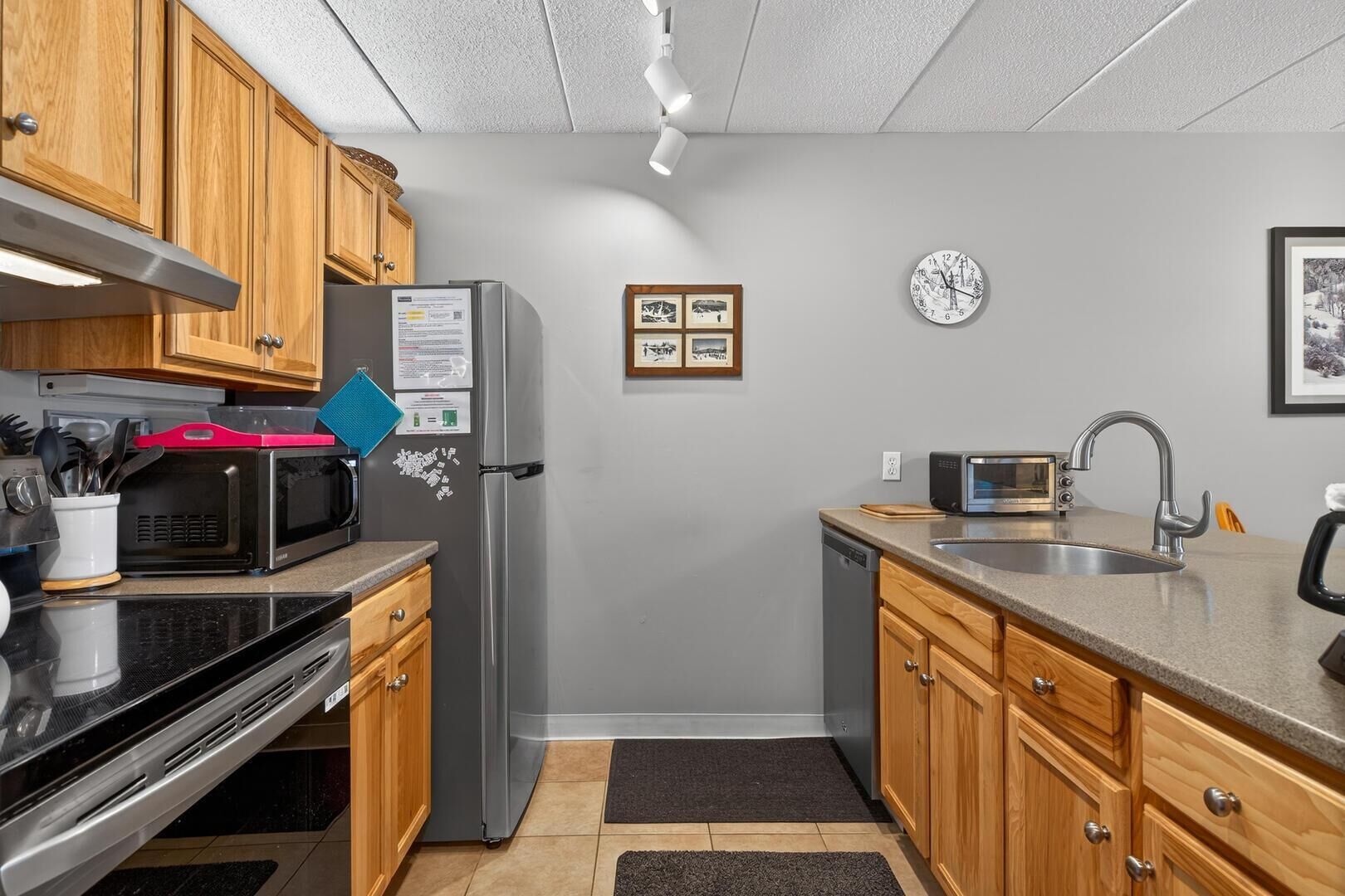 A compact kitchen with wooden cabinets, a stainless steel refrigerator, a microwave, a toaster, and a sink.