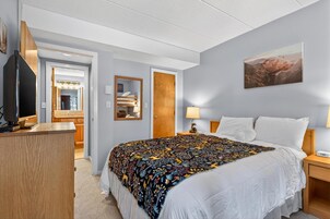 Habitación de hotel con cama, mesitas de noche, televisor, espejo y un cuadro en la pared.