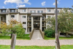 Un edificio residencial de varios pisos, con una entrada central, balcones y un paseo pavimentado.