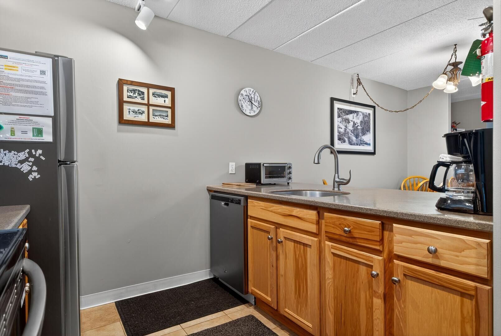 A compact kitchen with a refrigerator, microwave, toaster, sink, and wooden cabinets.