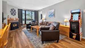 A cozy living room with a fireplace, a sofa, a coffee table, and a retro arcade machine. - Pinnacle E08 (Killington)