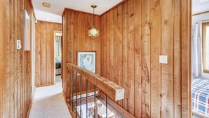 A wooden interior hallway with a staircase, a framed picture on the wall, and a ceiling light fixture. - Hemlock Ridge 1D (Killington)