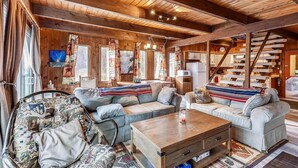 A cozy cabin interior with a wooden ceiling, a sofa set, a dining table, and a staircase. - Hemlock Ridge 1D (Killington)