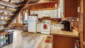 A kitchen with white cabinets, a stove, and a microwave. There is a wooden staircase leading to another level. - Hemlock Ridge 1D (Killington)