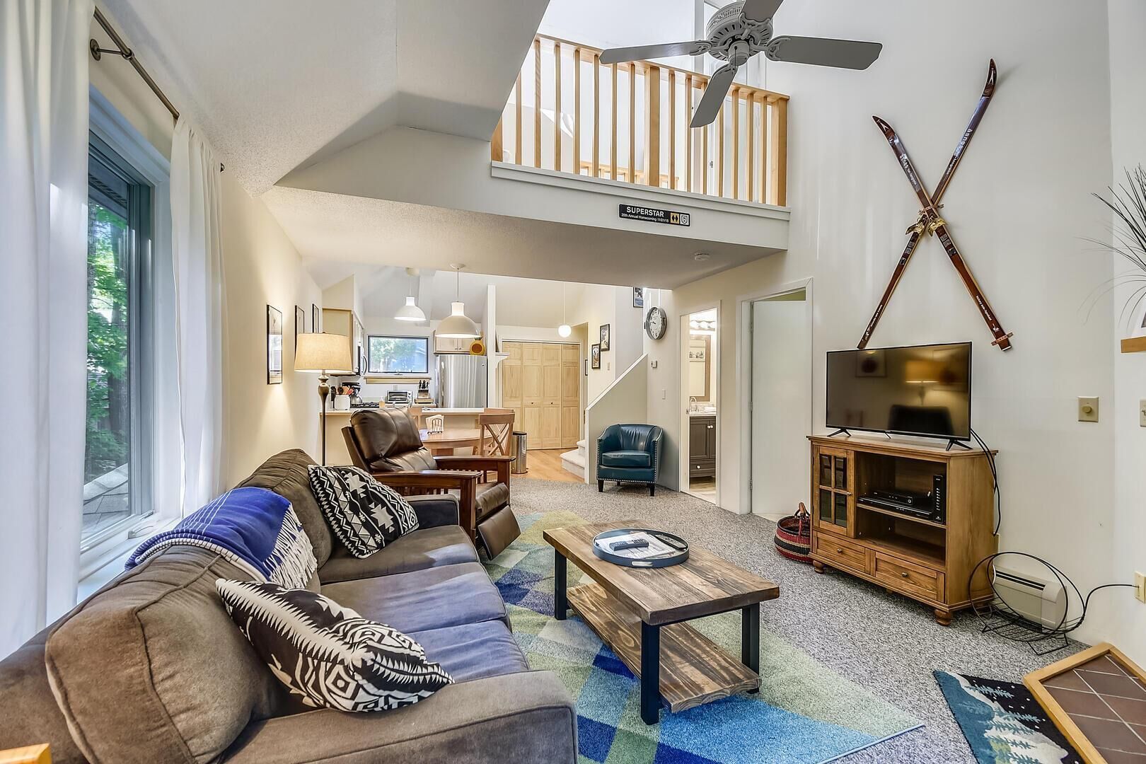 A spacious living room with a high ceiling, a balcony, and a TV on a wooden cabinet.