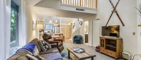 A spacious living room with a high ceiling, a balcony, and a TV on a wooden cabinet.