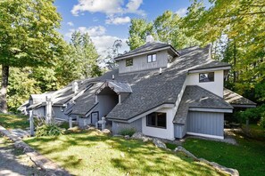 Une maison moderne avec un toit en pente, plusieurs niveaux et un jardin bien entretenu.