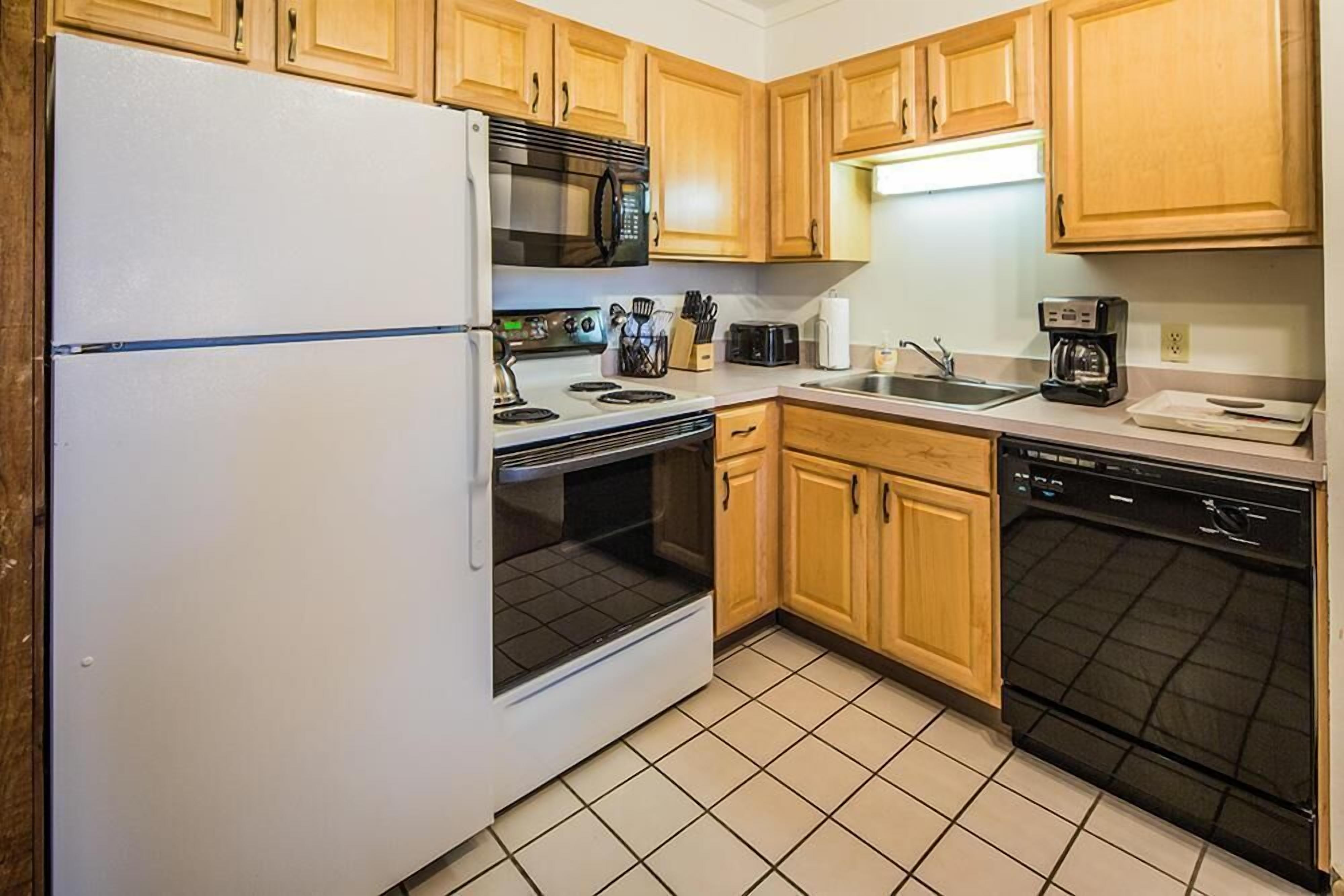 A compact kitchen with wooden cabinets, a white refrigerator, a microwave, a stove, a sink, and a dishwasher.