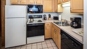 A compact kitchen with a white refrigerator, black microwave, stove, and dishwasher. - Whiffletree A5 (Killington)