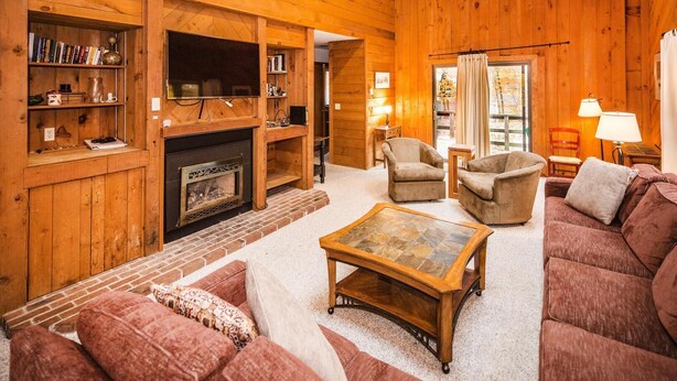 A cozy log cabin interior with a fireplace, a television, and a comfortable seating area. - Hideout Chalet (Killington)