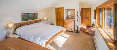 A bedroom with a large bed, wooden headboard, two bedside tables with lamps, a dresser, a coat rack, and a window with a view.