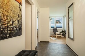 A hallway with a dark-toned bench, a large abstract painting, and a mirror on the right wall. - Apartment "Sunny" with Mountain View, Wi-Fi & Private Terrace (Bregenz)