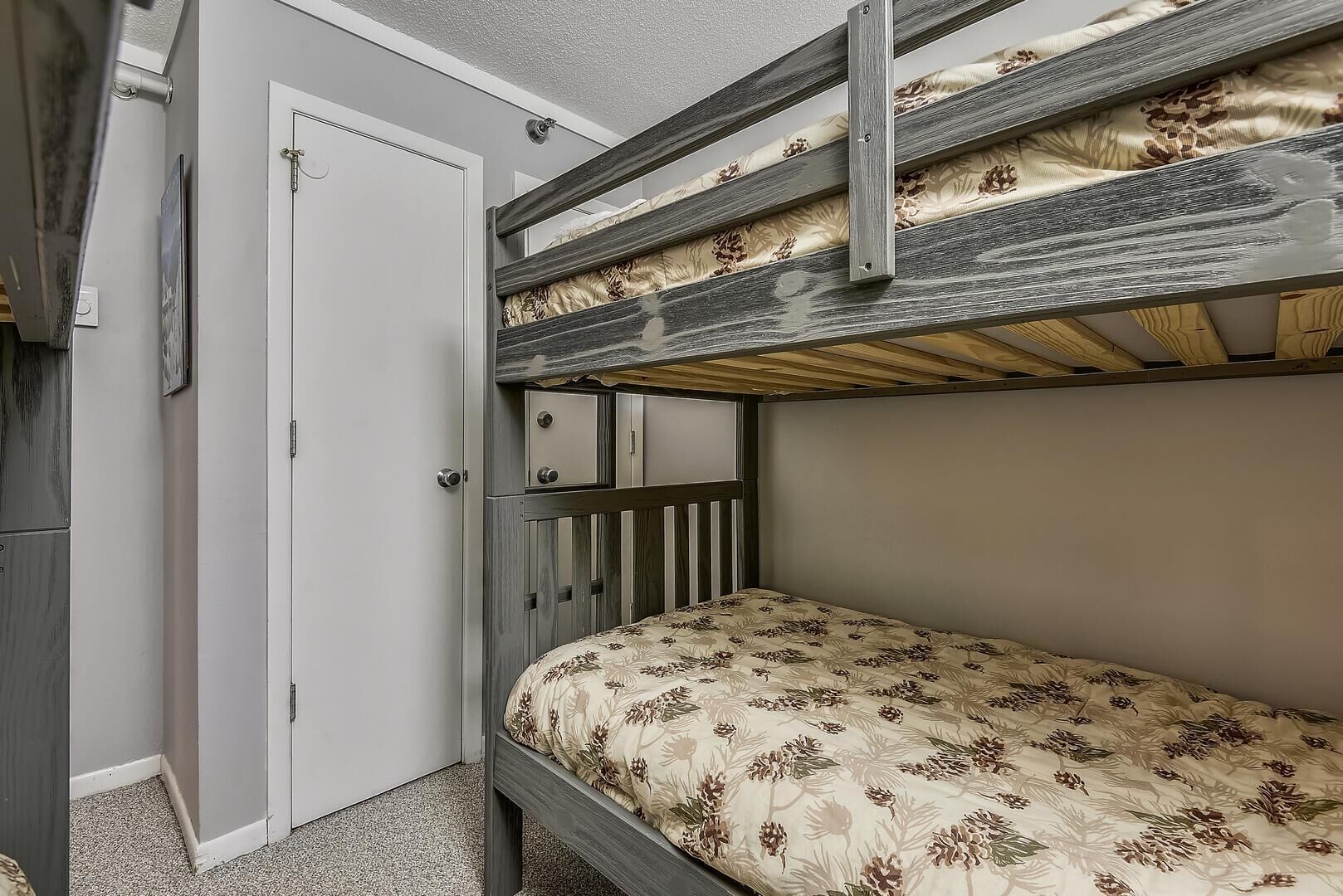 A bunk bed with a floral-patterned mattress, a white door, and a small cabinet with drawers.