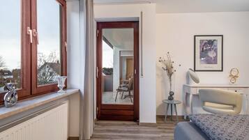 Ein Schlafzimmer mit Bett, Schreibtisch, Stuhl, Fenster und einer Tür, die auf einen Balkon führt.