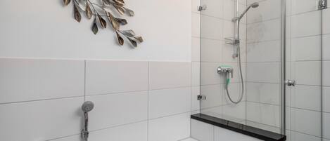 Un baño moderno con cabina de ducha de vidrio, bañera y una obra de arte decorativa con forma de hoja metálica en la pared.