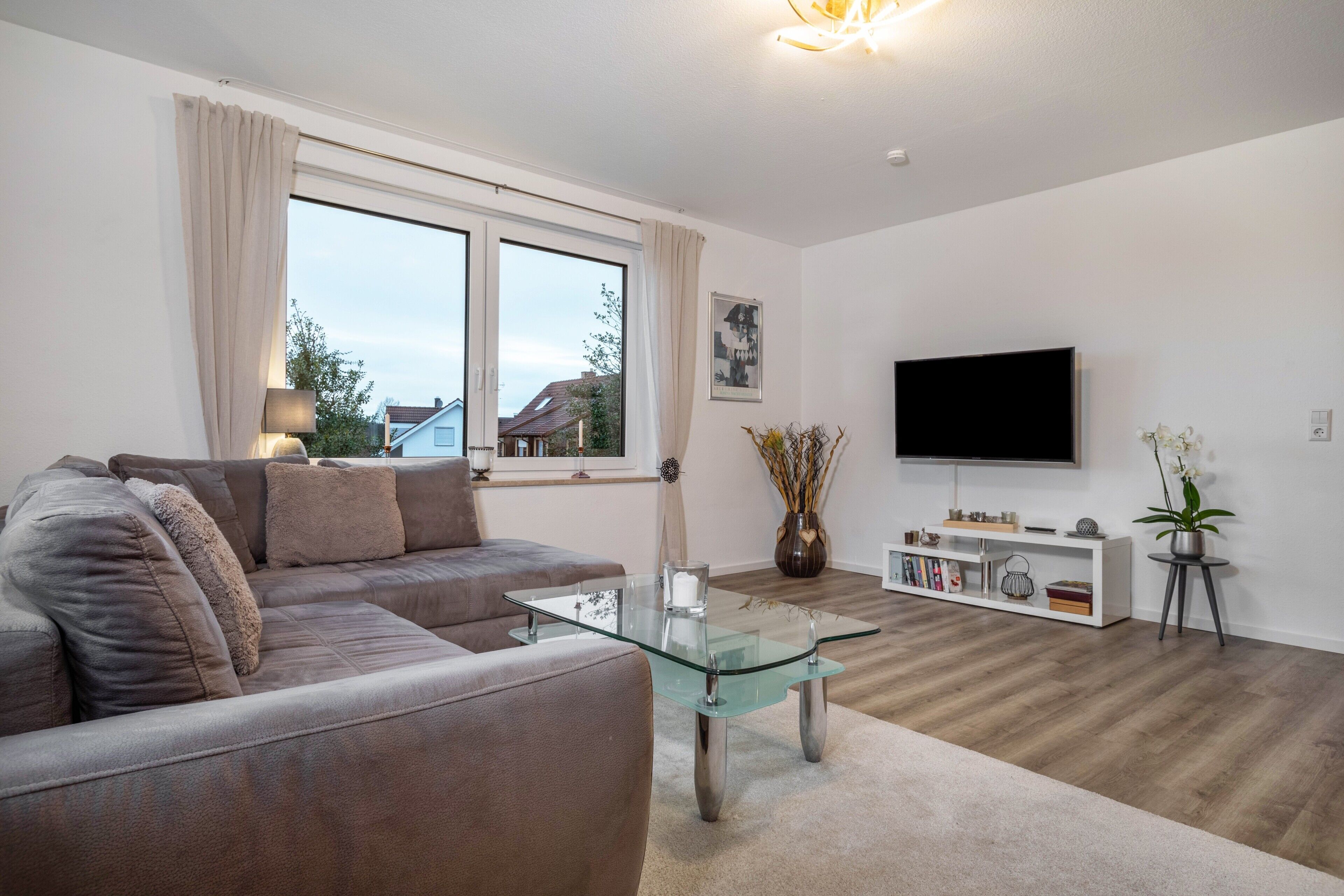 Ein modernes Wohnzimmer mit Glastisch, einer Couch, einem Fernseher und einem Bücherregal.