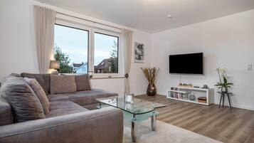 Ein modernes Wohnzimmer mit Glastisch, einer Couch, einem Fernseher und einem Bücherregal.