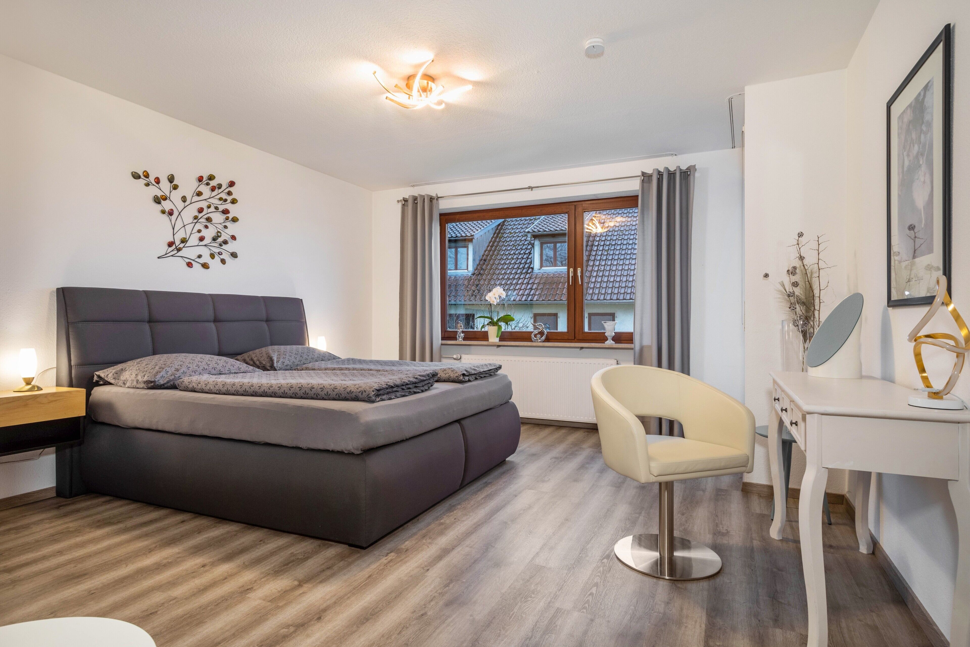 A modern bedroom with a bed, bedside table, chair, desk, and window with curtains.