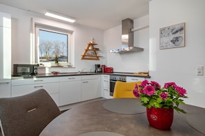 A modern kitchen with white cabinets, a microwave, a stove, and a window with a view of trees.