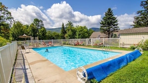 Une piscine rectangulaire entourée d’une clôture blanche et de chaises longues, le tout bordé d’une pelouse et d’arbres.