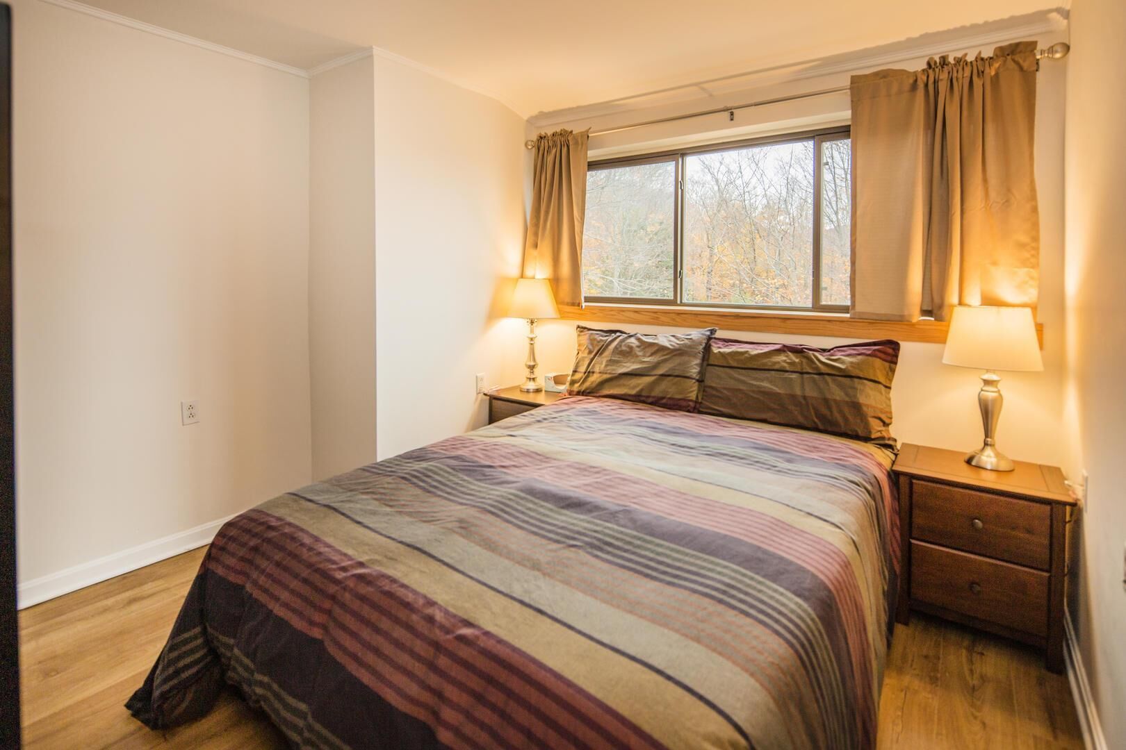 Une chambre avec un grand lit, deux tables de chevet, une fenêtre avec des rideaux et une lampe de chaque côté.