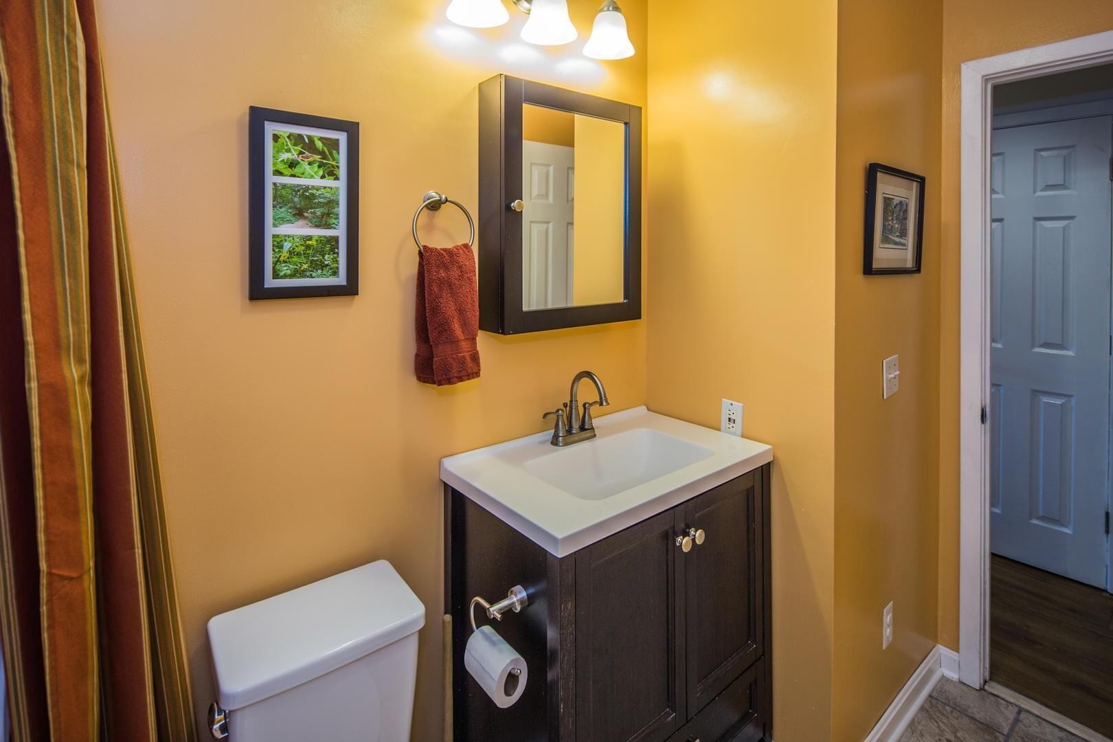 A bathroom with a white sink, dark cabinets, a toilet, and a mirror.