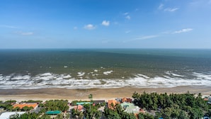 A coastal view with a beach, ocean waves, and a town with buildings and trees. - Stephen Luxury Apartments (Ho Chi Minh City)