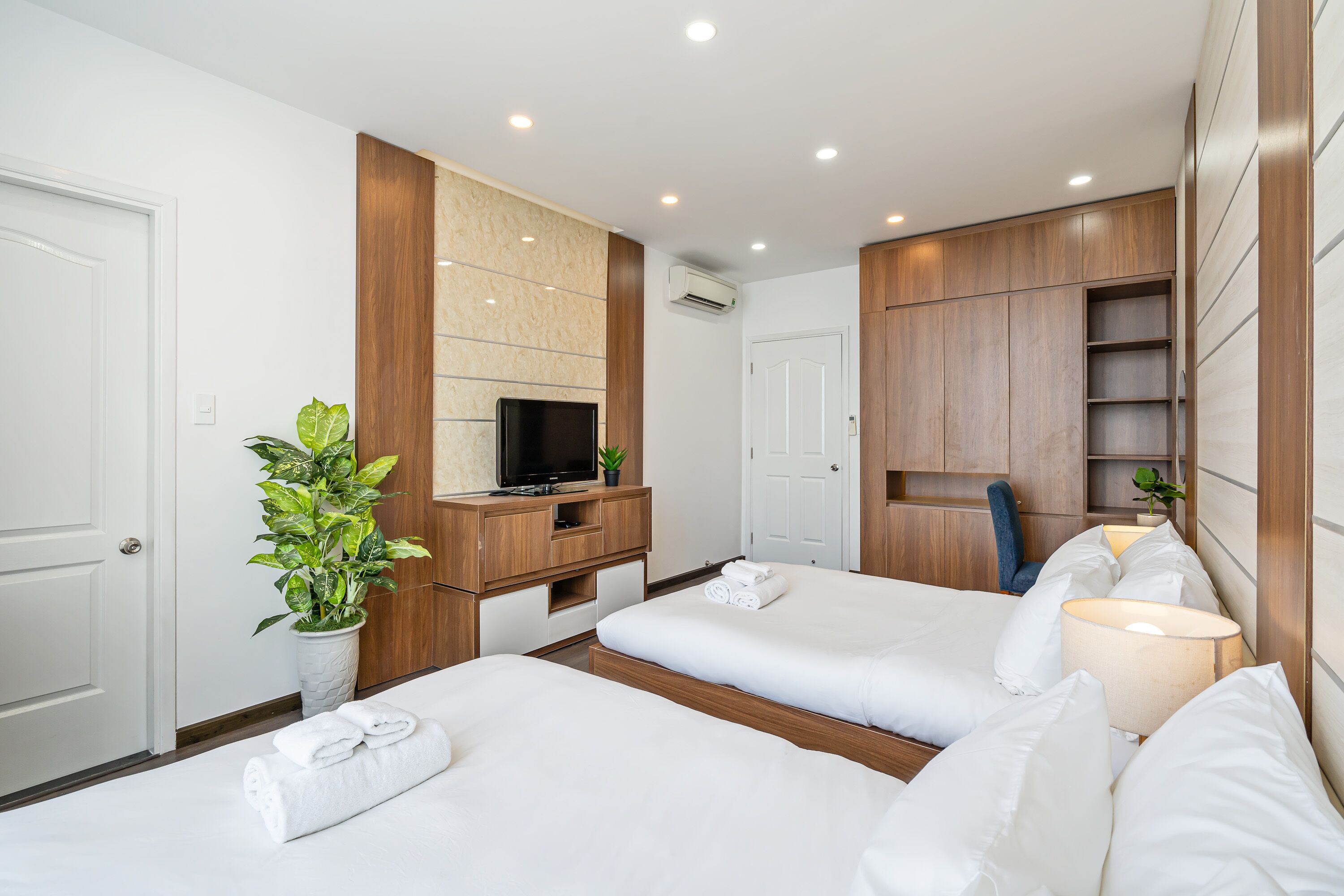 A hotel room with two beds, a TV, a desk, and a plant.