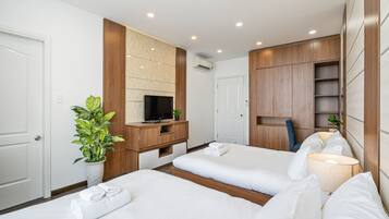 A hotel room with two beds, a TV, a desk, and a plant.