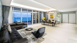 A modern living room with a large sectional sofa, a coffee table, and a dining area with chairs and a table. There is a large window with a view of the ocean. - Stephen Luxury Apartments (Ho Chi Minh City)