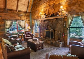 Un acogedor interior de cabaña de madera con sofás de cuero, una chimenea de piedra y un ventanal con vistas al exterior.