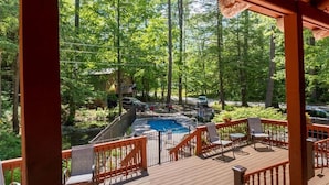 A wooden deck with a pool and chairs, surrounded by trees.
