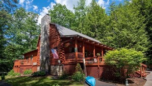A log cabin with a stone chimney, a porch, and a flag.