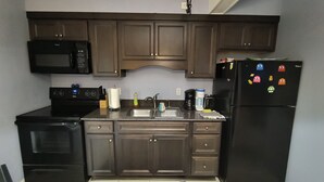 Una cocina con gabinetes de madera oscura, un microondas negro, un refrigerador negro con imanes, una estufa y una cafetera.