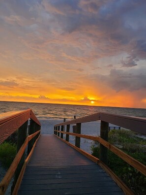A wooden boardwalk leading to the ocean with a sunset in the background. - It's all about location and you deserve a vacation (St. Pete Beach)